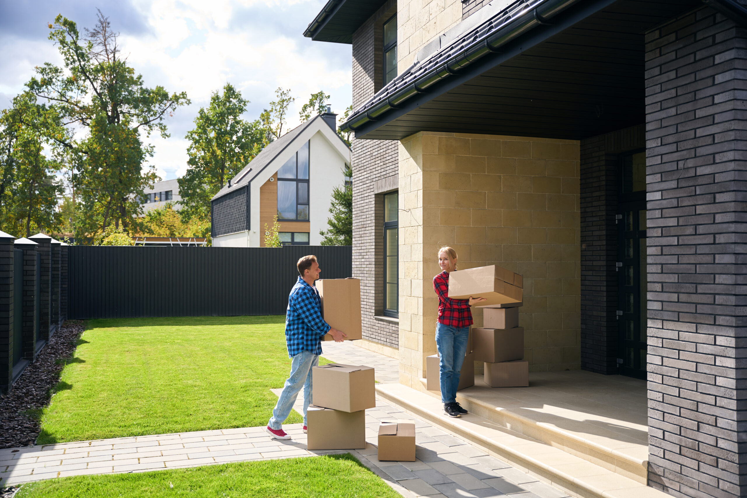 Full length picture of contented couple walking towards house entrance while holding boxes in hands