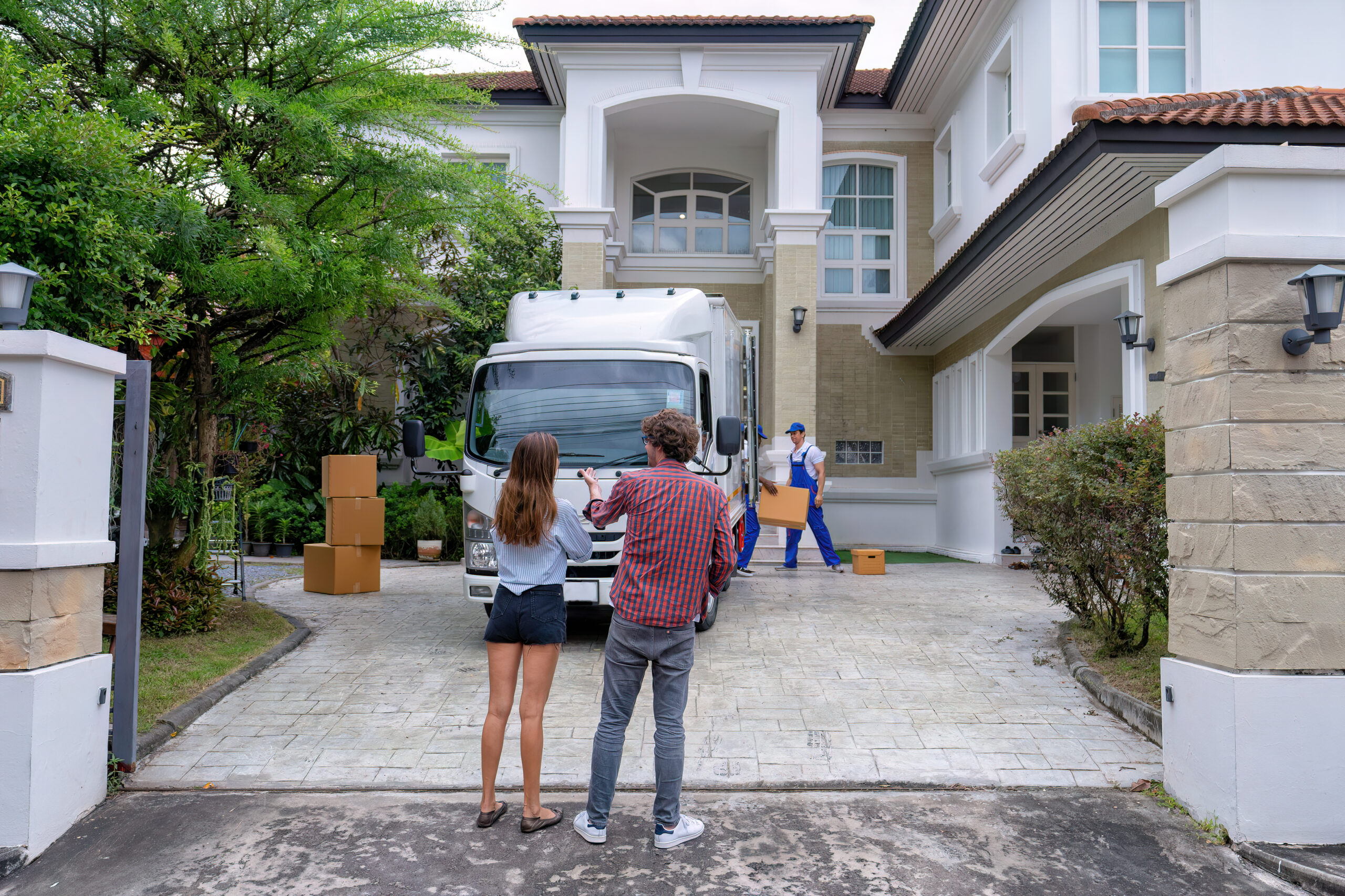 Young couple lover just move in the new house and proud for they purchased house happy look around at the truck of goods mover service team